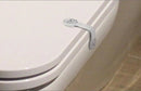 A white toilet seat features a child safety lock with a smiling face design, ensuring the lid is child-proof. The floor is tiled.