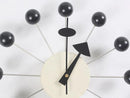 A contemporary wall clock, named Clock, background wall, wall clock, features a light-colored circular face with black hands. Metal rods extend from it, ending in black spheres, mimicking an atomic model—ideal for minimalist European style interiors.