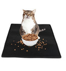 A waterproof cat litter pad cat sits upright on a black Cat Litter Pad Honeycomb Cat Pad Waterproof Urine Proof Pad behind a white bowl of dry food, with kibble scattered around. The waterproof mat contrasts sharply with the plain white background.