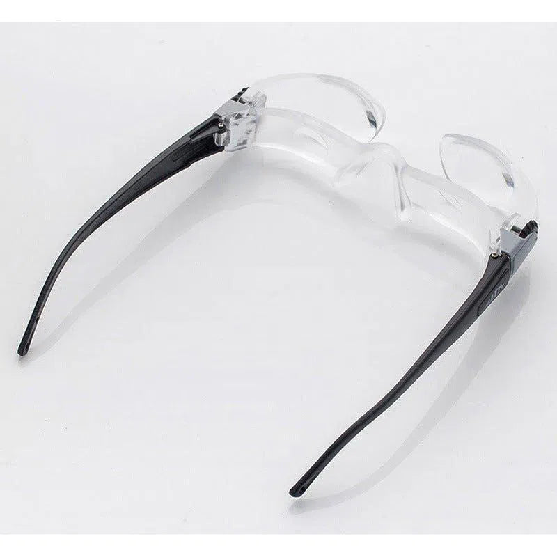 The 2.1X Diopter 3 Foldable 300 Degrees MaxTV Binocular TV Screen features a flexible hinge and provides hands-free 2.1X magnification for close-up tasks with transparent lenses and black arms, positioned upside down on a white surface.