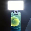 A mobile phone features the Mini Selfie Fill Light—an LED lamp with 3 color modes and adjustable brightness—clipped on top, brightly illuminating a dimly lit area for enhanced photography.