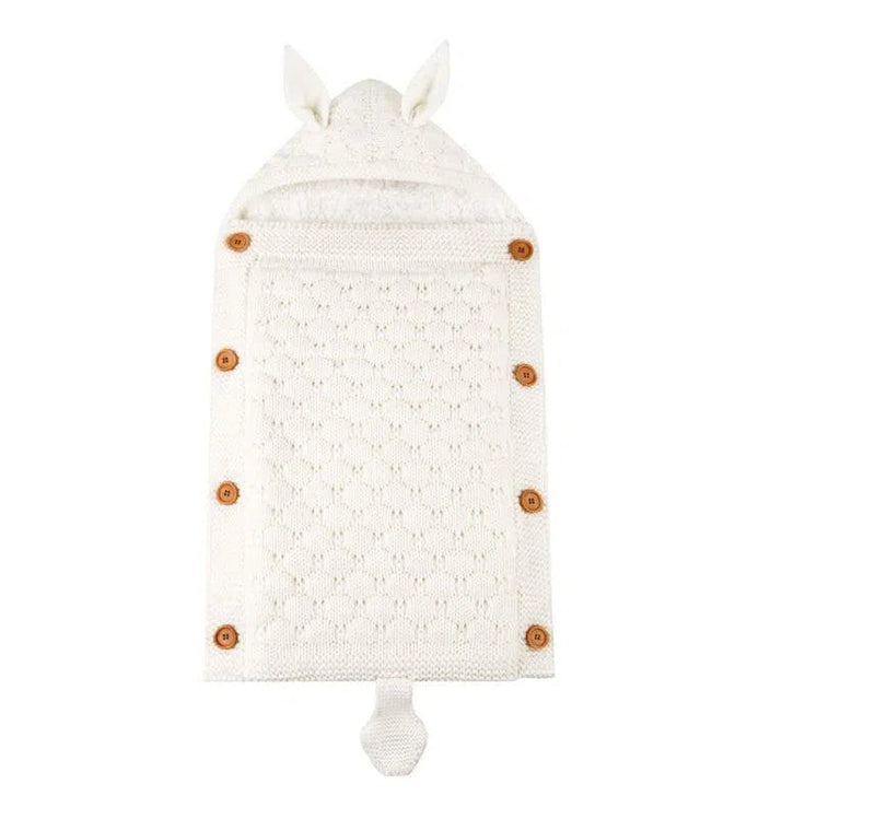 A cream-colored, knitted Baby Sleeping Bag with a hood, tiny ears, and a tail features a diamond pattern and wooden buttons. It is made with lamb cashmere lining and is displayed flat on a plain white background.