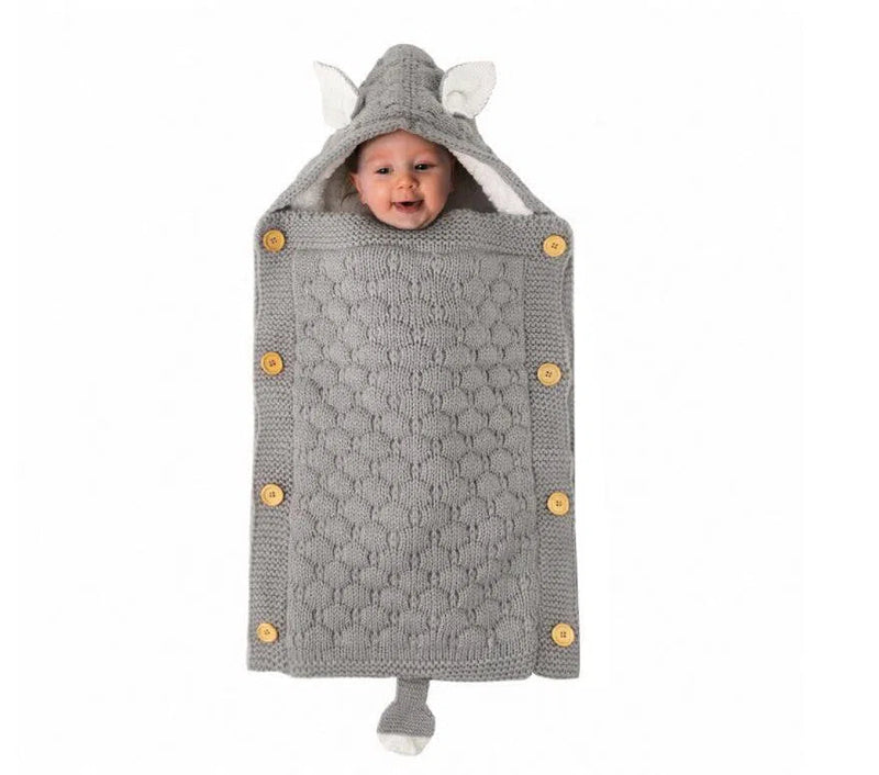 A baby smiles wrapped in a cozy gray knit Baby Sleeping Bag, resembling a mouse. It features ears on the hood, button accents, a tail at the bottom, and lamb cashmere lining for comfort.