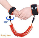 An adult and child are connected by an orange coiled safety strap with black and orange wristbands. The Child Safety Wristband has anti-slip Velcro and a 360° Rotary Head label, highlighting its swivel feature.