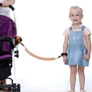 A smiling young girl in a blue denim dress enjoys security with a Child Safety Wristband featuring an orange link. Nearby, a purple stroller offers 360-degree rotation as an adult grips the handle against a plain white background.