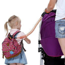 A child with a pink backpack and an adult, both wearing denim, are connected by an orange Child Safety Wristband with 360-degree free rotation. The adult pushes a stroller with a purple canopy.