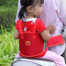 A young child sits on an adult, both outdoors amidst greenery. The vibrant red Child Safety Rope motorcycle child safety belt with reflective strips enhances visibility and security.