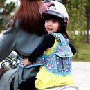 A child in a colorful star-patterned Child Safety Rope Motorcycle Child Safety Belt and a pink helmet happily rides on an adults scooter. The gray-coated adult, with their back to the camera, navigates through a backdrop of trees.