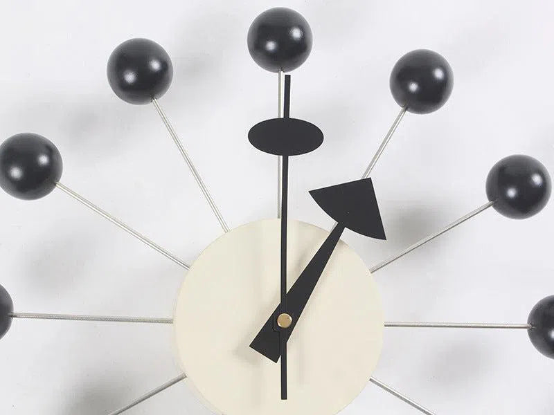 A contemporary wall clock, named Clock, background wall, wall clock, features a light-colored circular face with black hands. Metal rods extend from it, ending in black spheres, mimicking an atomic model—ideal for minimalist European style interiors.