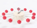 A chic European-style wall clock features red spheres on metal rods representing numbers, forming a circle around a sleek white cylindrical base. Silver minimalist hands complete the design, perfect for modern interiors.