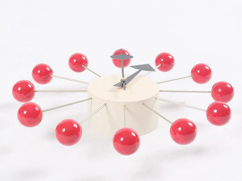 A chic European-style wall clock features red spheres on metal rods representing numbers, forming a circle around a sleek white cylindrical base. Silver minimalist hands complete the design, perfect for modern interiors.