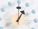 The Clock, background wall, wall clock showcases a European-style modern abstract design with a beige face and black hands. Its twelve blue spheres connected by rods resemble sun rays or atomic structures, ideal for enhancing interior design against a white background.