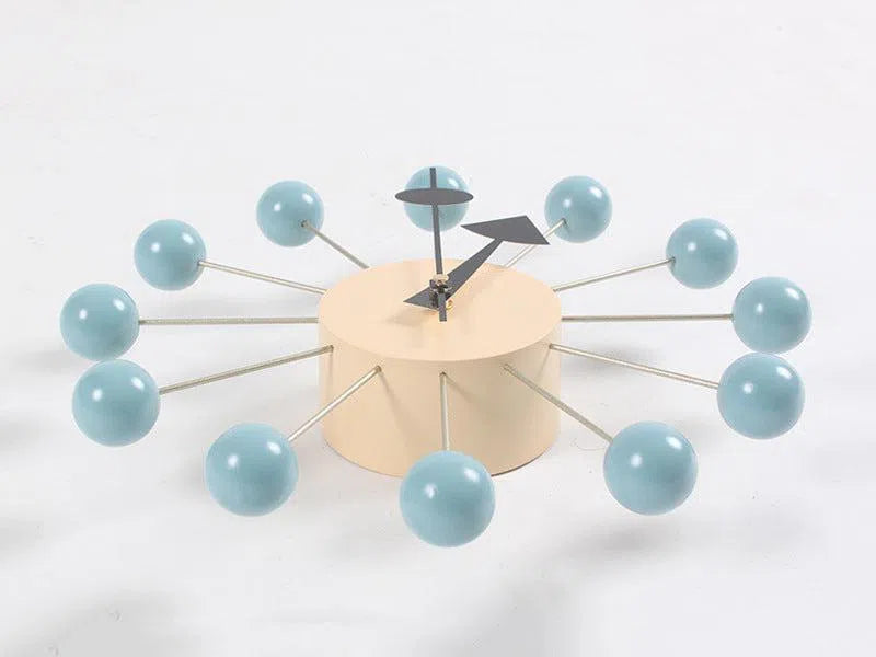 A modern European-style wall clock with a minimalist design features a beige cylindrical base, blue spheres at rod ends as hour markers, and black hands. This Clock, background wall, wall clock enhances any interior effortlessly.