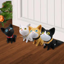Four cartoon-style cat figurines with big eyes and collars, available in black, white, yellow, and black-and-white, serve as door stoppers on a wooden floor. Behind them is a white door with a potted plant to the left. Product: Door Handle Punch-free Door Stop Cute Cat Door Stopper Anti-collision.