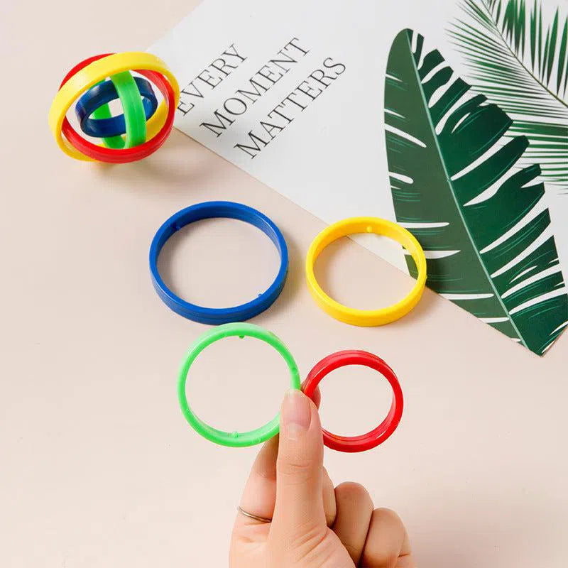 A hand holds colorful Fingertip Gyro Creative Leisure Inertia Rotation rings above a beige surface, ideal for enhancing hand-eye coordination. Nearby are more rings and intersecting structures. A card reading EVERY MOMENT MATTERS with a green leaf design partially shows, emphasizing focus.