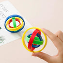 A hand holds a Fingertip Gyro Creative Leisure Inertia Rotation, featuring interlocking rings in red, green, blue, and yellow—a great stress-relief gadget. Another identical puzzle is on the table next to a pamphlet with green leaf illustrations.