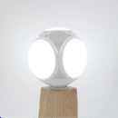 The Foldable Leaf Light Football Light LED Light features a spherical design with four glowing circular panels on a wooden base against a plain white background. Its minimalist style accentuates energy-efficient lighting, promoting a modern and sustainable aesthetic.