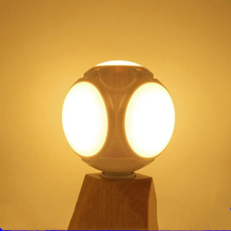 The Foldable Leaf Light Football Light LED Light, featuring spherical design and oval-shaped LEDs, emits a warm yellow glow. It stands on a wooden base, delivering energy-efficient lighting and creating a cozy atmosphere against a plain backdrop.