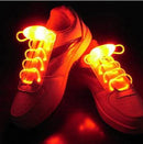 The Led Sport Shoe Laces Glow Show Strings Round Flash Light Shoelaces illuminate a pair of white sneakers with glowing orange fiber-optic technology, creating an eye-catching effect on a dark background.
