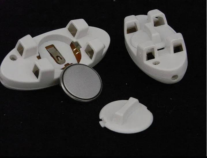 Two disassembled white electrical socket components with three slots each rest on a black surface alongside a round button cell battery, suggesting the unseen magic of fiber-optic technology possibly powering the LED Sport Shoe Laces Glow Shoe Strings Round Flash Light Shoelaces.