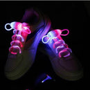 White sneakers with glowing neon shoelaces in the dark create a striking visual effect using fiber-optic technology. The Led Sport Shoe Laces Glow Shoe Strings emit vibrant pink and blue light.