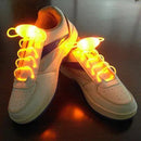 White sneakers with orange LED fiber-optic Led Sport Shoe Laces Glow Shoe Strings Round Flash Light Shoelaces glow on a dark surface, featuring stylish blue stripes on their sides.