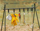 A black metal stand outdoors displays various items: a white mug, yellow gloves, garden shears, a metal ladle, a slotted spoon, and a spatula. Resembling an Outdoor Camping Aluminum Alloy Large Foldable Portable Clothes Drying Rack For Camping Travel Triangle, each item hangs on individual hooks.