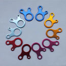 A circle of colorful aluminum alloy Outdoor Camping Snail Wind Rope Buckles sits on a gray background, arranged in a gradient from blue to orange to red to pink, each featuring two upper loops and one larger round opening.