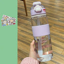 A hand holds a Portable Large Capacity Plastic Cup, featuring a transparent body with a purple lid and grip for all your hydration needs. The scene includes a wooden floor backdrop and two decorative sticker sheets on the left.
