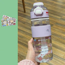 A hand holds the adorable Portable Large Capacity Plastic Cup, featuring a clear design with a lavender lid and cartoon animal decals. It complements colorful stickers on a green surface, adding charm. Its wooden floor setting highlights its style and practical temperature resistance.