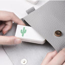 A person slips a compact Portable pill storage box featuring a green cactus illustration into an open light gray textured purse with a metallic button clasp.