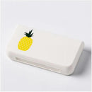 A Portable pill storage box in white plastic, rectangular in shape, featuring a yellow pineapple graphic on its lid, is placed on a light gray surface.