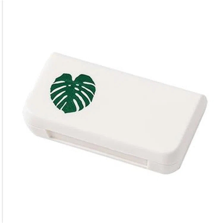 This stylish portable pill storage box features a white rectangular case with a green monstera leaf design on the lid.