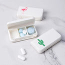 Two white Portable pill storage boxes, one with a flamingo and the other with a cactus design, are open on marble. They hold round blue and white pills, with two white pills outside—perfect for stylish travel.