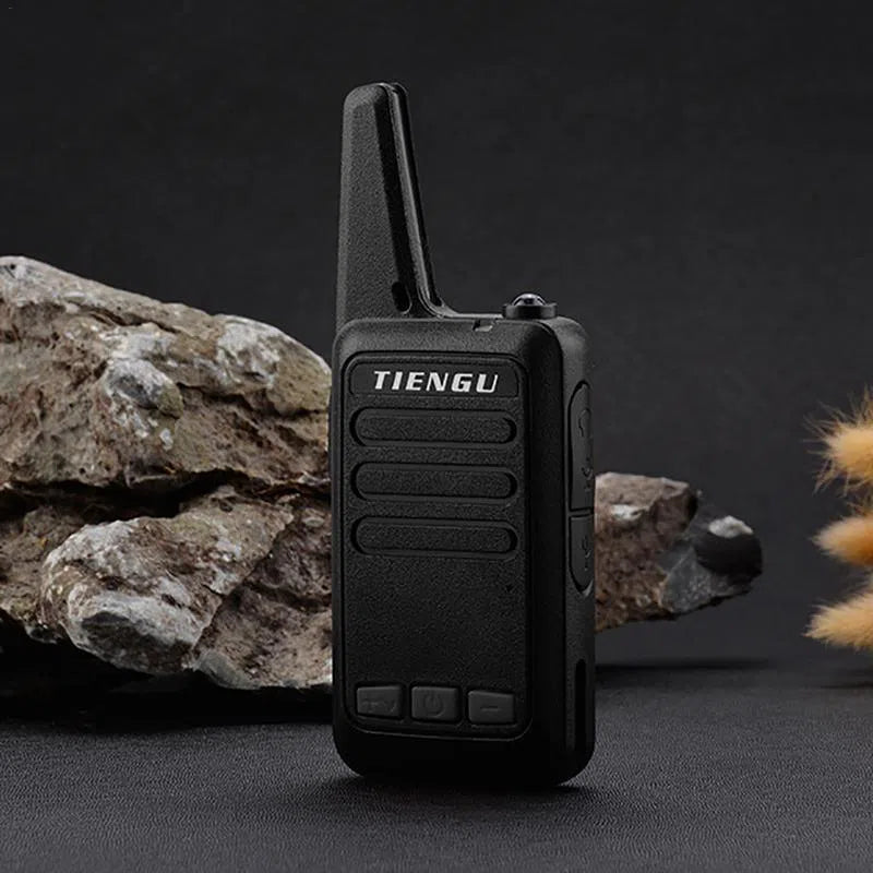 A compact TIENGU Professional Wireless Handheld Intercom Radio is shown on a dark background with rocks and small plants. The black two-way radio has buttons, a short antenna, and an Android USB interface for easy charging.