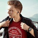 A man stands outdoors with mountains behind him, wearing TWS innovative simple wireless Bluetooth headset for high-quality sound. He adjusts his black jacket, complementing his red Lee Cooper shirt proudly labeled for sustainable production.