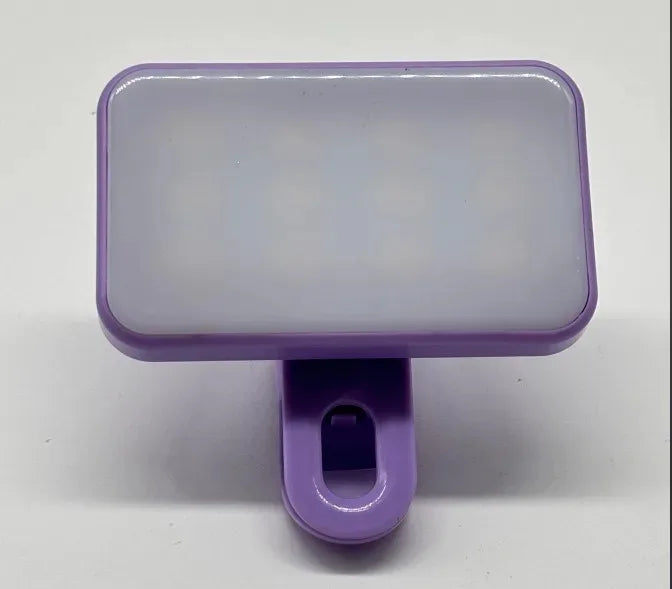 The Mini Selfie Fill Light is a compact, rectangular purple LED lamp with 3 color modes, adjustable brightness, a white diffused front panel, and rechargeable clip-on design for phones or computers. Shown on a plain white background.